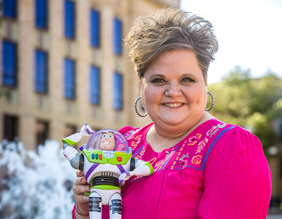 Administrative Assistant Melissa Sodalak holding Buzz Lightyear figure against a blurred building