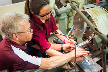 man teaching female student how to machine parts