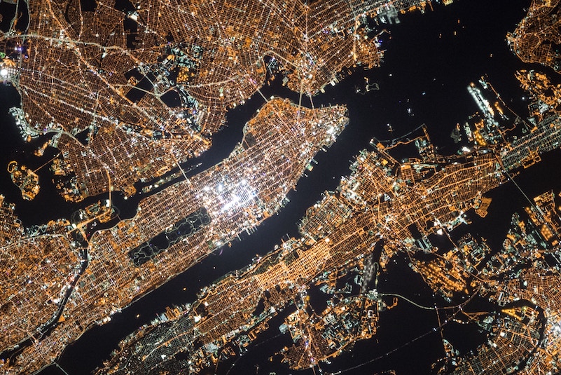 satellite image of New York City taken at night with lights from above shining brightly