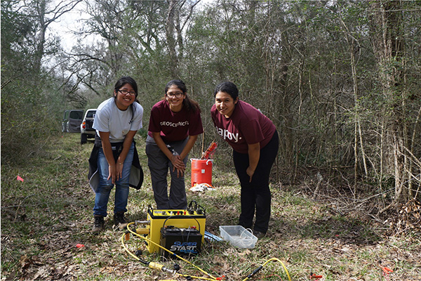 three students standing over geology equipment in forest