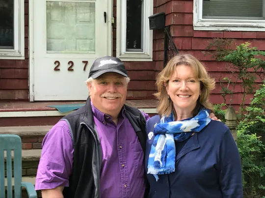 Carolyn Timbie posing with her husband in front of a home built with red panels.