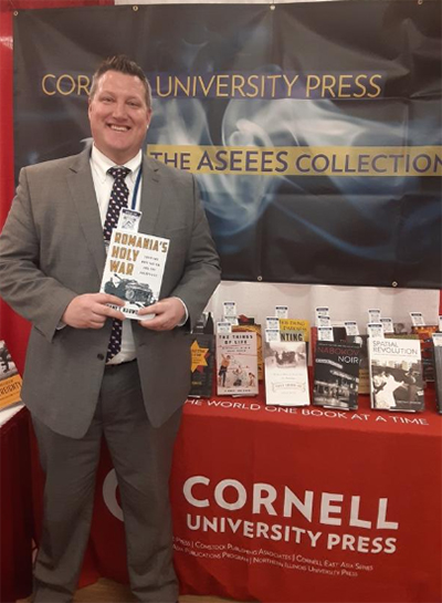 Grant Harward holding his book with a Cornell University Press backdrop behind him