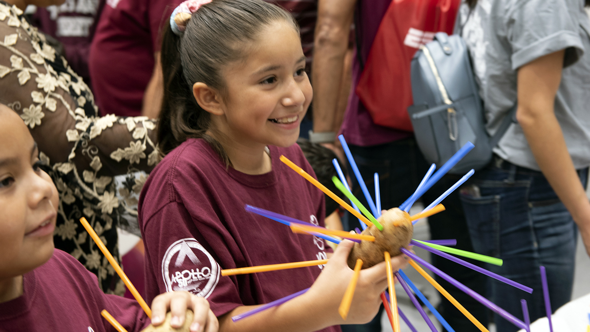 two young girls holding a potato with straws stuck in them