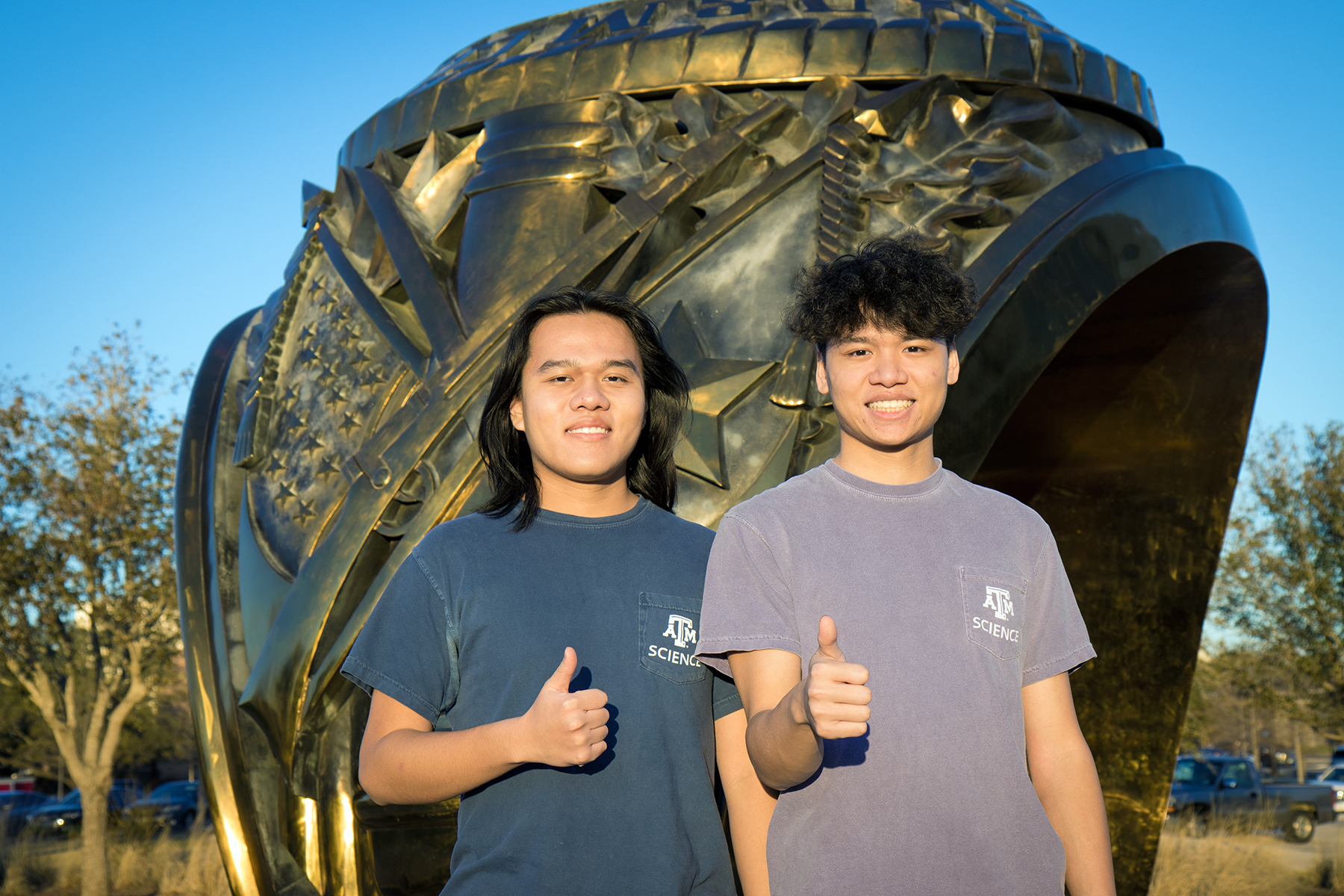 Texas A&amp;M biology majors and brothers Henry and Kyle Nguyen flash a classic gig 'em in front of the Aggie Ring sculpture on the Texas A&amp;M campus