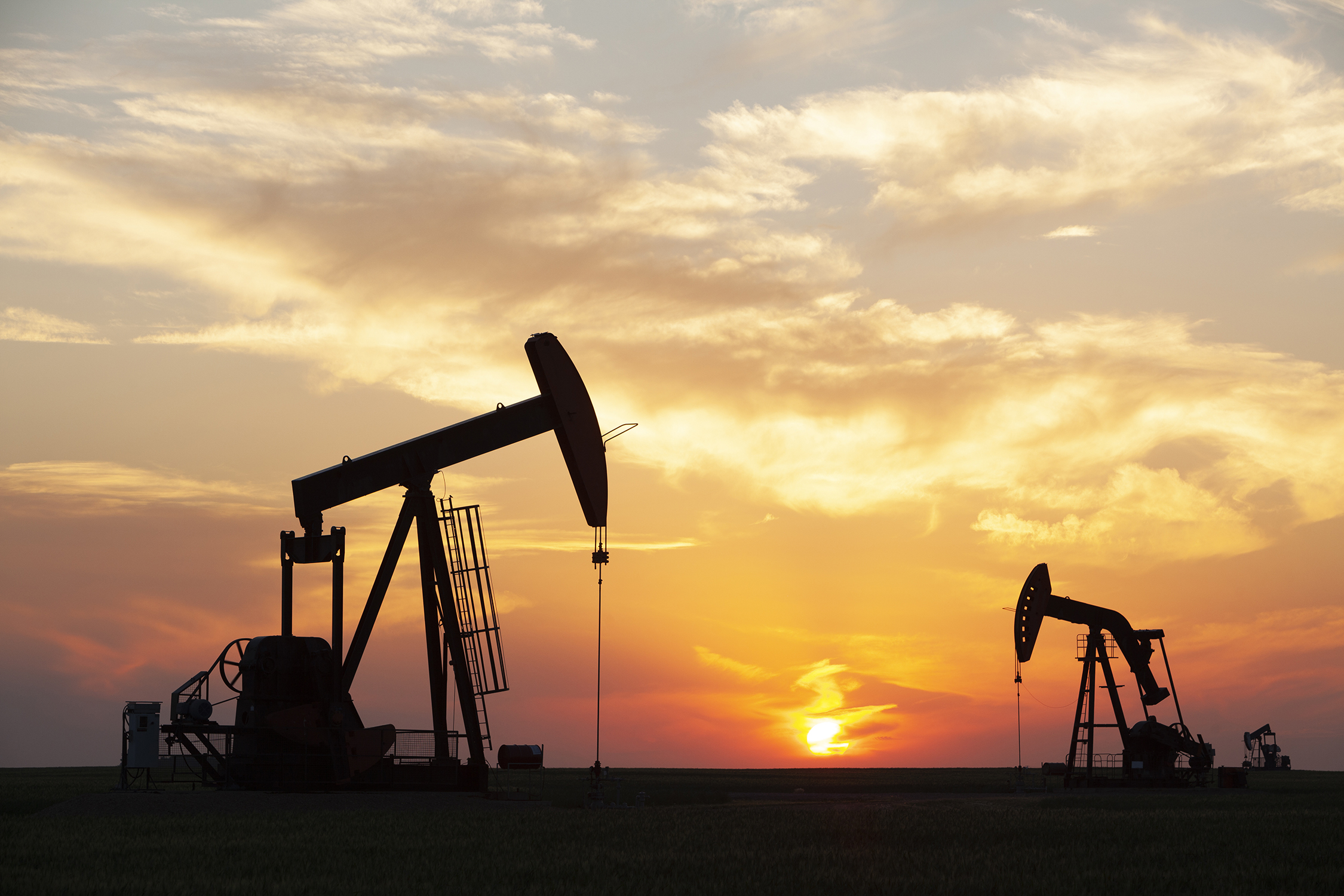 Pump jacks working in the field against a sunset backdrop