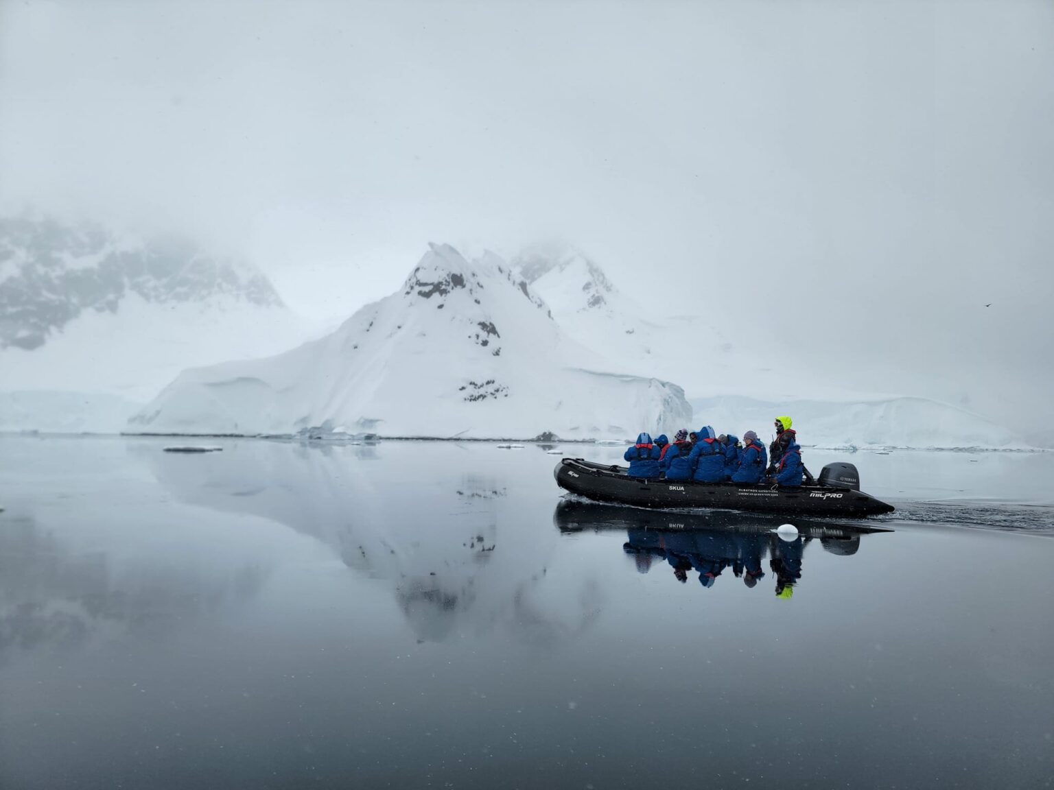 A small group of students, faculty and staff ride in a boat with snow-covered mountains in the background while on expedition during Texas A&amp;M University's first study abroad trip to Antarctica in late fall 2023