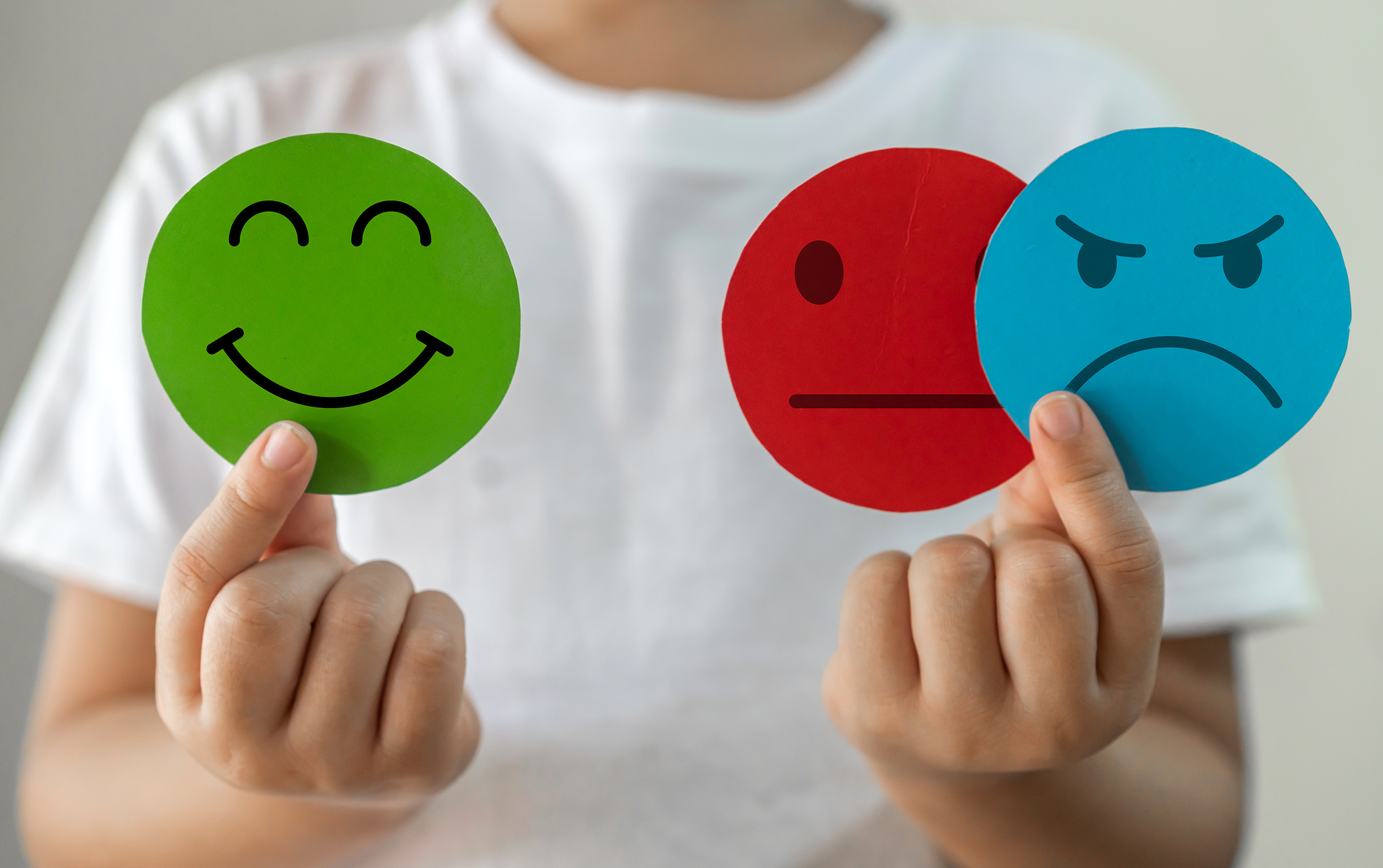 Child's hands holding colored paper cutout circles depicting different facial expressions and emotion, including happiness, ambivalence and anger