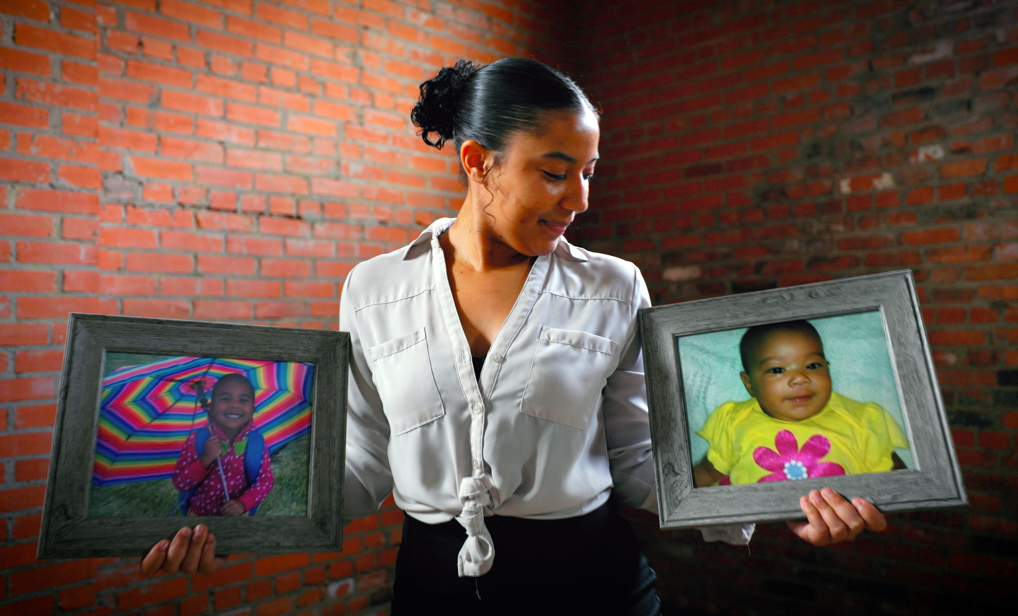 Aria Vargyas poses with her arms outstretched from both sides, each holding a framed photograph of her younger sisters and career inspirations: Karrina in her right arm and Sydnee in her left. Both sisters were among the 24 fatalities in the 2013 Moore tornado.