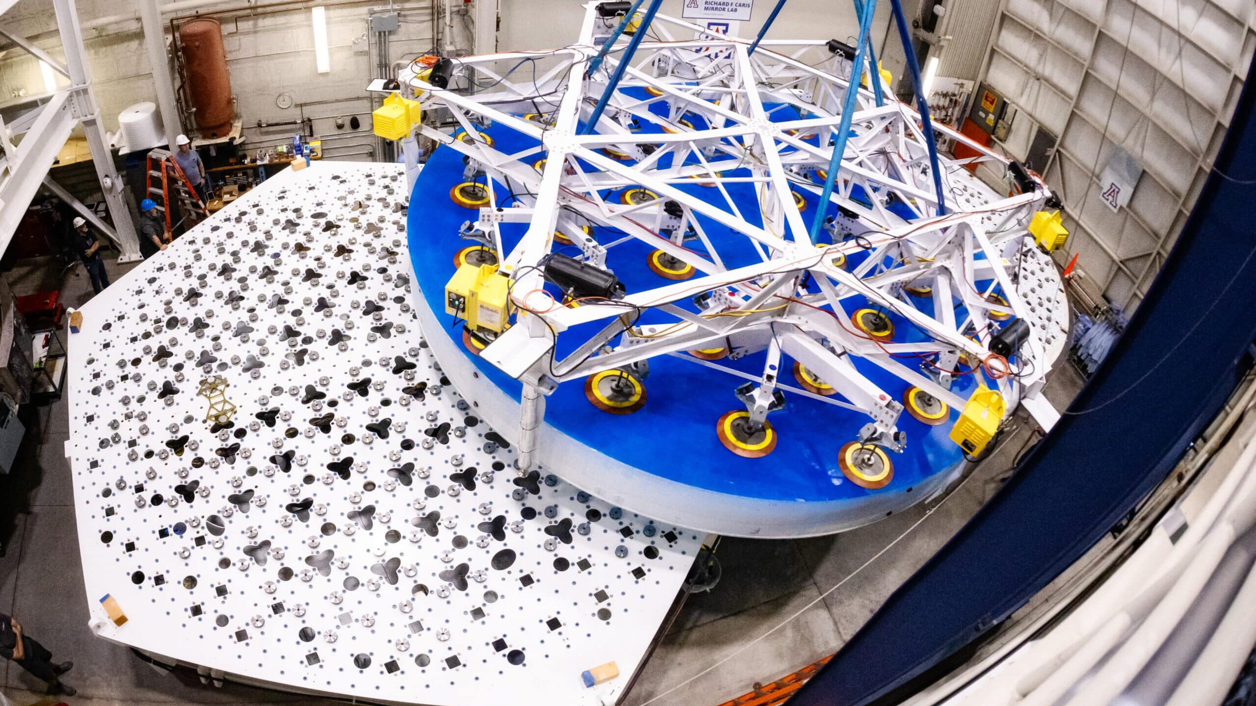 Overhead view of a completed 8.4-meter-diameter primary mirror transport and placement for the Giant Magellan Telescope suspended above the support system prototype at the University of Arizona’s Richard F. Caris Mirror Lab