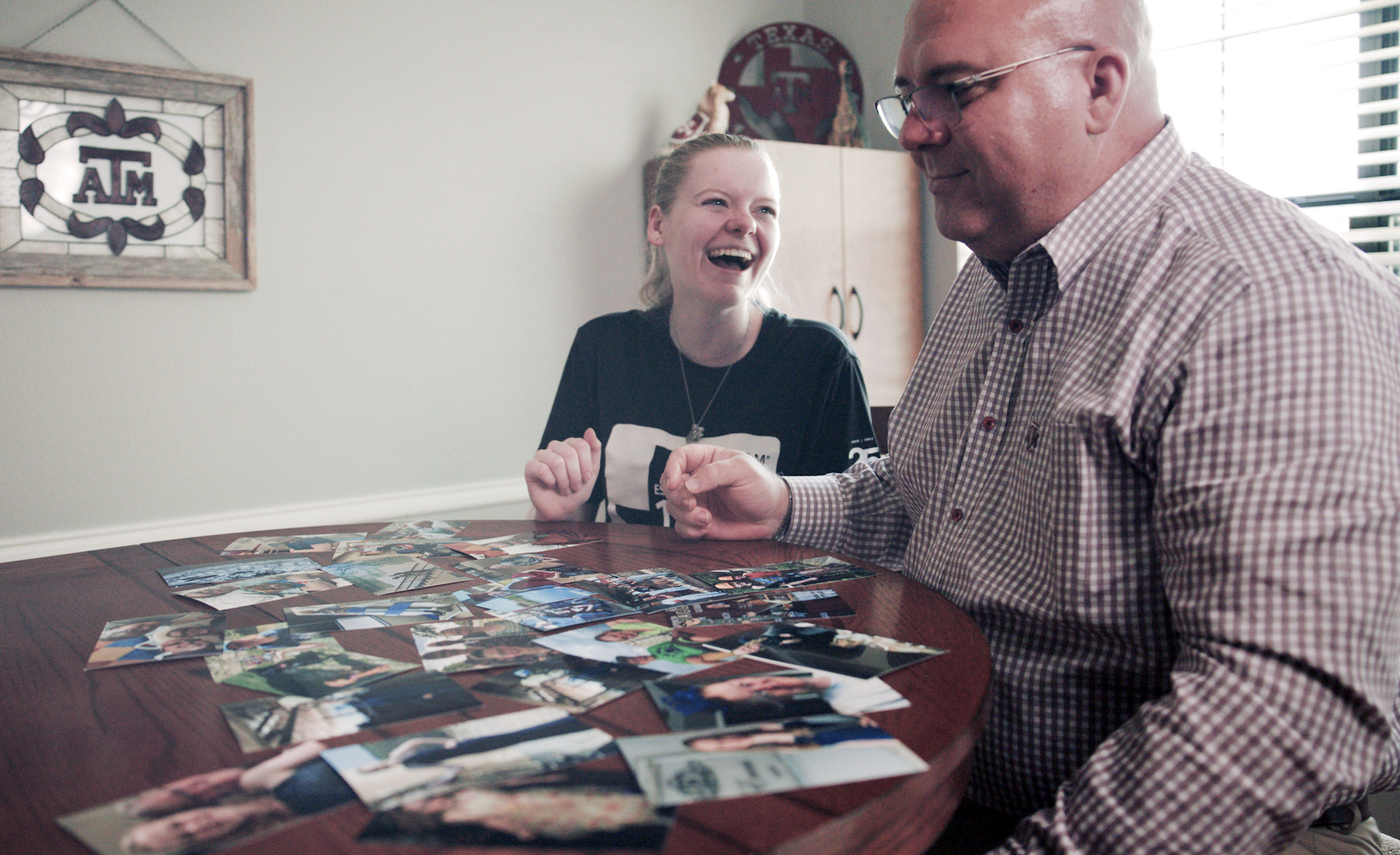 Texas A&amp;M University allied health major Abbi Evans laughs while sitting with her dad, Ed Evans, at a kitchen table and looking through photographs spread out across the table