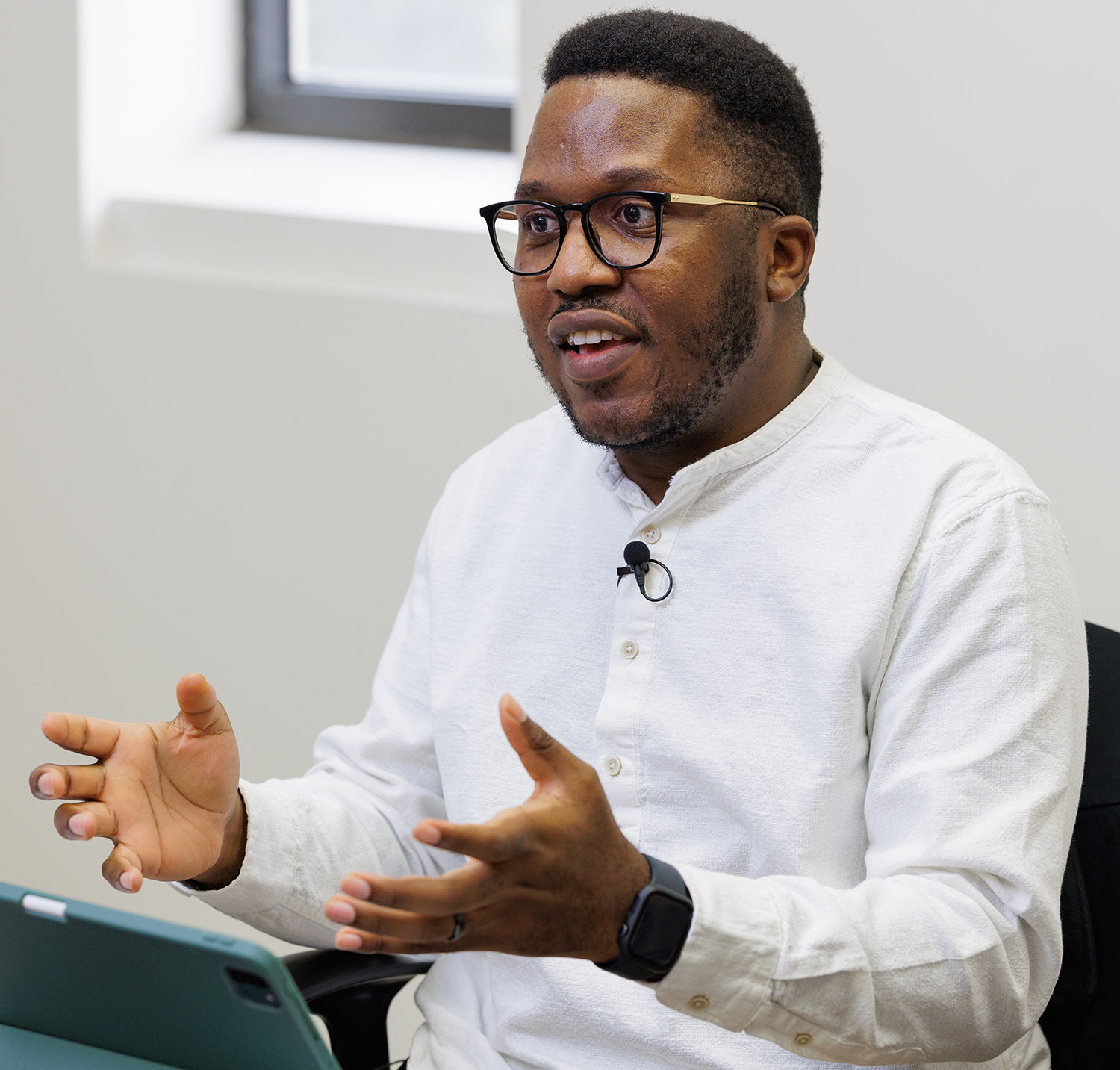 Dr. Lucien Nana Yobo in a white shirt and glasses gesturing during a discussion in an office setting.