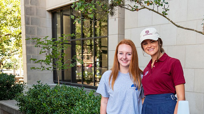 Two female students posing for a photograph in front of a university building