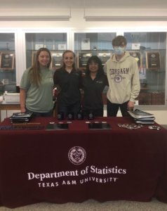 4 ambassadors stand behind a table with a maroon statistics tablecloth