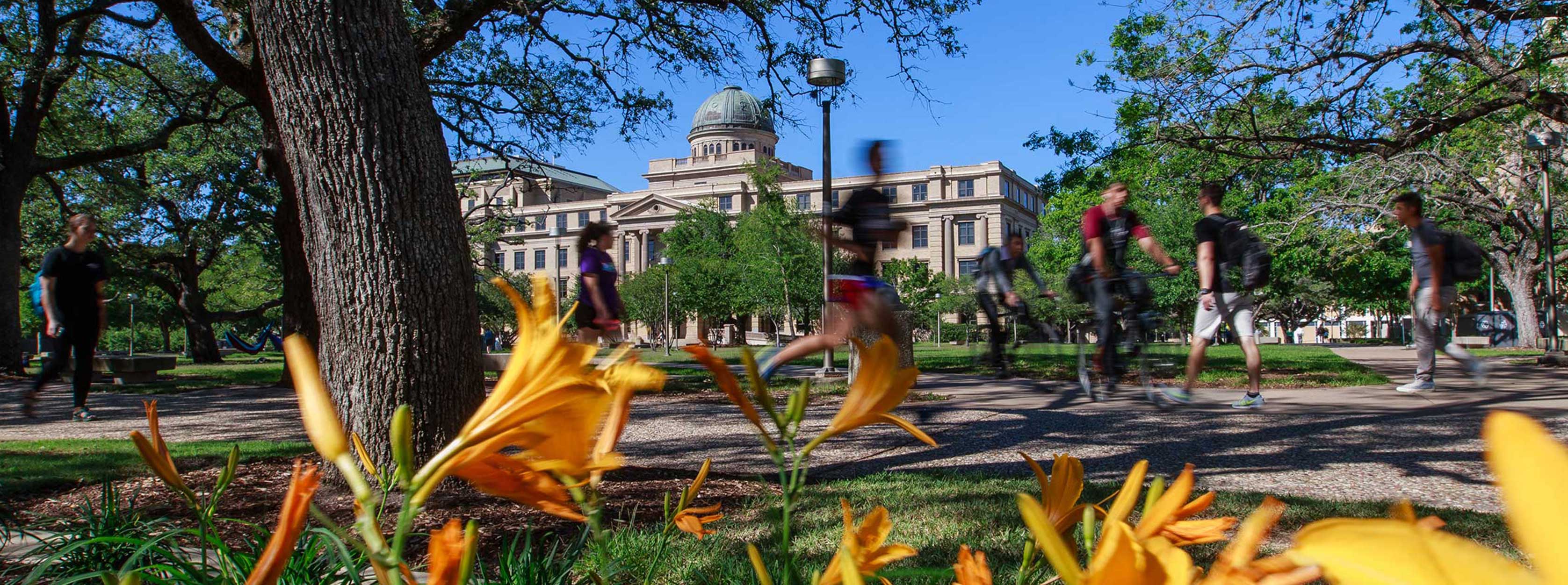 photo of Texas A&amp;M academic building during springtime with white logo in the middle of the image that reads "legacy through leadership"