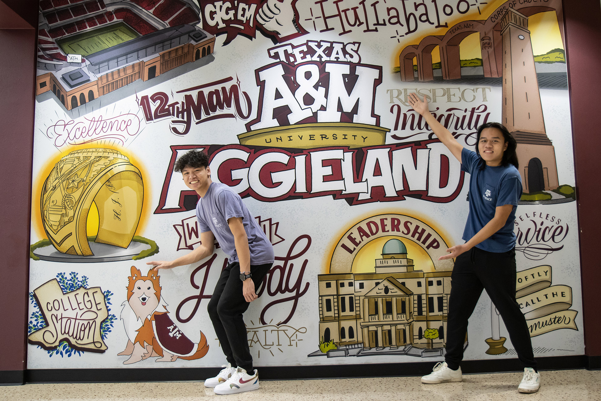 two young asian men standing in front of mural depicting all symbols of Texas A&amp;M university